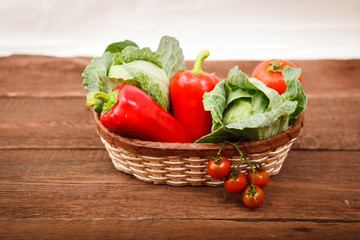 Basket with fresh vegetables on a wooden table. Tomatoes, Bulgarian pepper and cabbage.