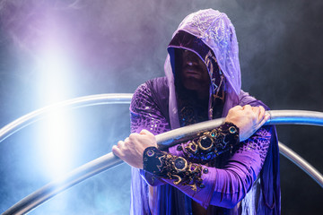 Fairy-tale character assassin in a purple cloak with a hood with two large cross wheel