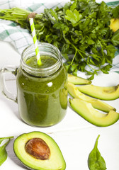 Freshly blended green smoothie in a glass with straw. White wooden background.