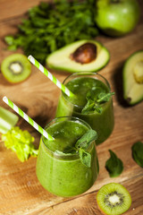 Freshly blended green smoothie in glasses with straws. Wooden background.