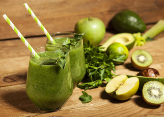 Freshly blended green smoothie in glasses with straws. Wooden background.