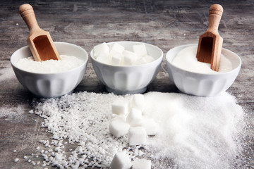 Bowl with white sand and lump sugar on grey background