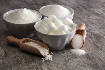 Bowl with white sand and lump sugar on grey background
