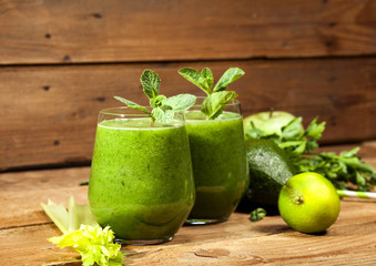 Freshly blended green smoothie in glasses with straws. Wooden background.