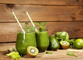 Freshly blended green smoothie in glasses with straws. Wooden background.