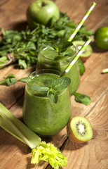 Freshly blended green smoothie in glasses with straws. Wooden background.