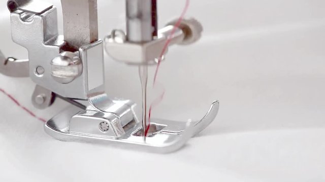 Close-up of the Foot of the Sewing Machine Making the Seam with Red Thread along the White Fabric. Selective Focus is on the Foot.  In the end of video the Fabric Closing the Screen. Copy Space.
