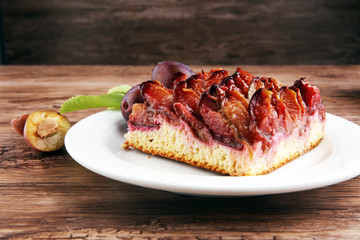 rustic plum cake on wooden background with plums around