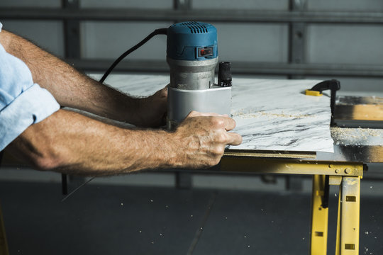 A man using a woodworking router to trim a laminate table top