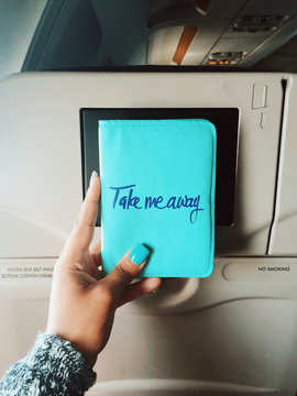 A woman holding up her passport wallet that says Take me away" on the front"" woman holding up her pass"