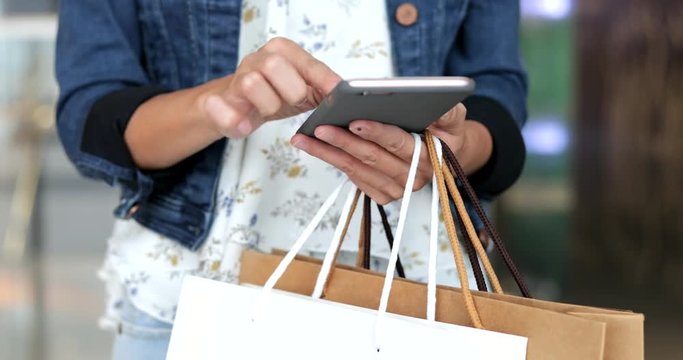 Woman holding many shopping bags and using smart phone
