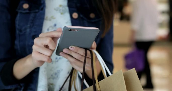 Woman holding shopping bags and using smart phone
