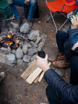 Hip group sitting outdoors around campfire with coffee and leather boots