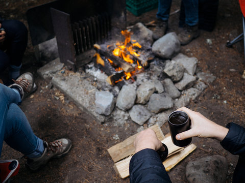 Young man holding coffee mug near campfire while camping