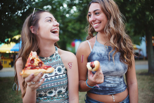 Two young friends eating pizza and hot dogs at a carnival