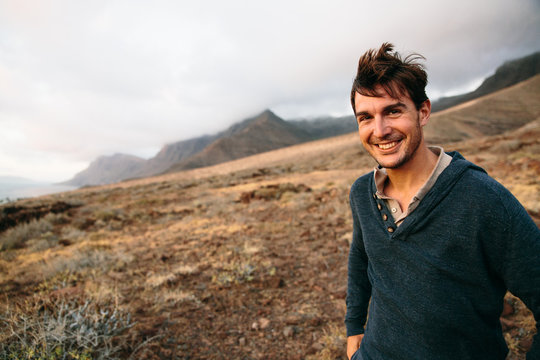 Handsome brunet with windy hair smiling at camera against of landscape