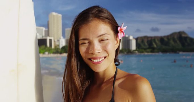 Smiling young woman with surfboard at Waikiki Beach. Beautiful female tourist is on summer vacation at island in Honolulu. She is wearing bikini top against buildings and sky.