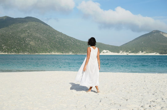 Back view of woman in white at the beach looking at the sea