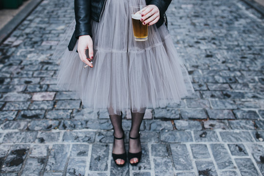 Fashionable woman standing on street with glass of beer and cigarette