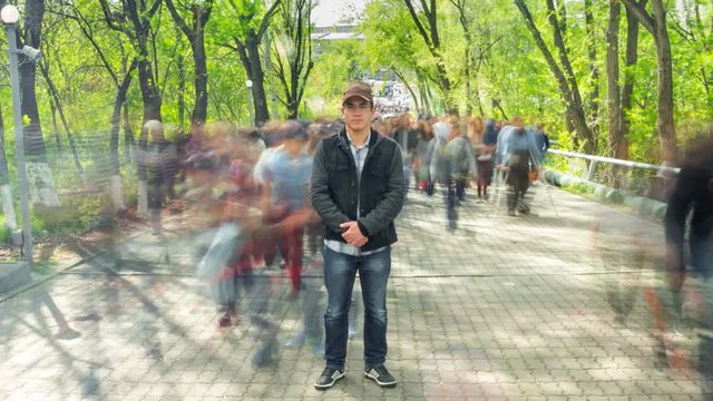 Man standing alone in blurred crowd, on background green trees. Time Lapse. The camera moves away