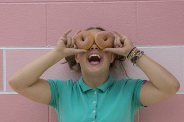 Teenage girl being silly holding two donuts over her eyes.