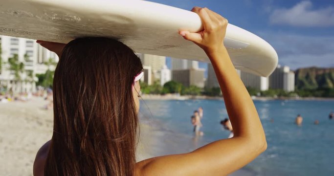 Young woman carrying surfboard on head at Waikiki Beach. Female tourist with long brunette hair is walking on shore during summer vacation. She is enjoying at island in Honolulu.