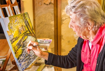 Senior woman painting at her easel, in her studio in France.