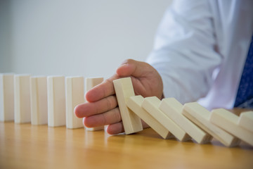 Businesswoman Hand Stopping Dominoes From Falling On Office Desk. Risk Prevention Concept