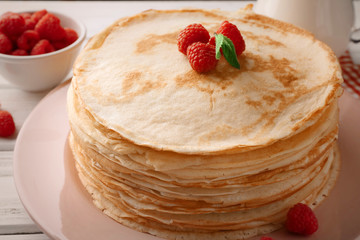 Stack of thin pancakes served with raspberry on pink plate