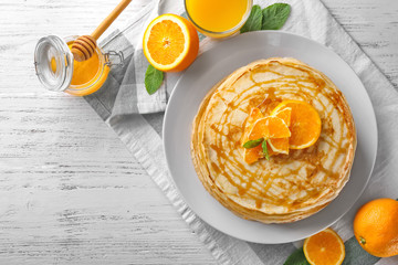 Stack of thin pancakes served with honey and orange slices on white plate