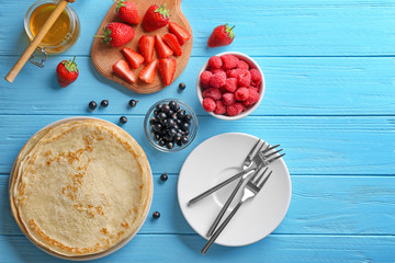 Composition with thin pancakes, honey and berries on blue wooden table