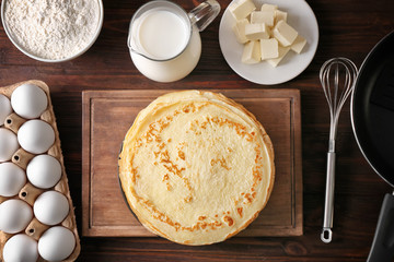 Composition with thin pancakes, eggs, flour, milk and butter on wooden table