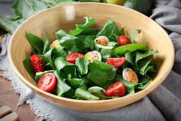 Salad with quail eggs and spinach in bowl on table