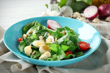 Salad with quail eggs and spinach in plate on table
