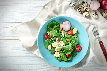 Salad with quail eggs and spinach in plate on table