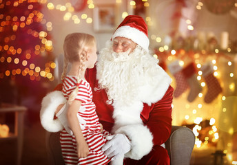 Fototapeta na wymiar Cute little girl sitting on Santa's lap in room with beautiful Christmas decorations