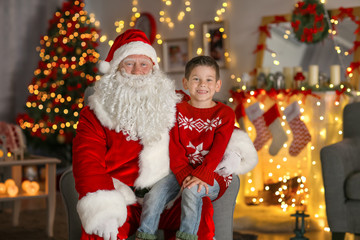 Fototapeta na wymiar Happy little boy sitting on Santa's lap in room with beautiful Christmas decorations