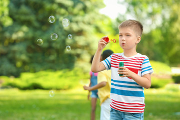 Cute little boy blowing soap bubbles outdoors