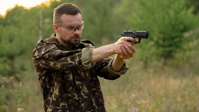 Young man in camouflage shooting from a gun, close up. Slow motion