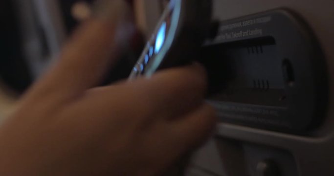 Close-up shot of a woman using control pad of seat monitor in the airplane. She changing some options and placing it back