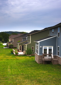 Backyard of a house shot looking sideways at other different color houses and backyards along with green grass and blue sky shot during daylight