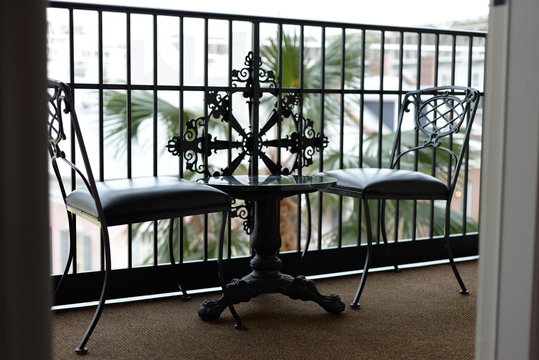 Two chairs and a table setup outdoor in a patio balcony of an apartment room shot from inside the room looking out during daytime