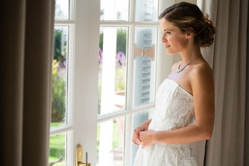 Side view of beautiful bride looking through window at home