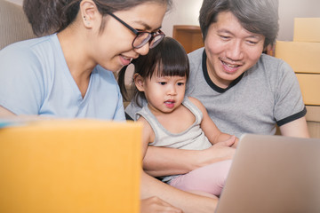 Portrait of a little girl with her parents using computer and unpacking boxes together