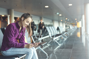 Girl at the airport window sits on the banch and looking at smartphone