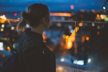 Young woman looking at evening city from skyscraper viewing platform