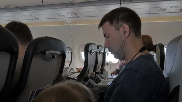 Young man listening to music on headphones via cell phone. A businessman during the flight is watching a video from a mobile phone, tablet. Business trip.