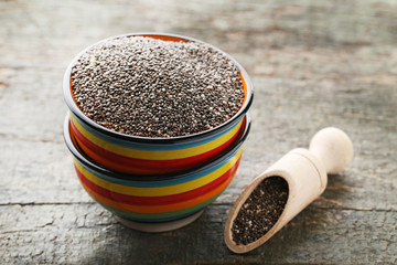 Heap of chia seeds in bowl and scoop on wooden table