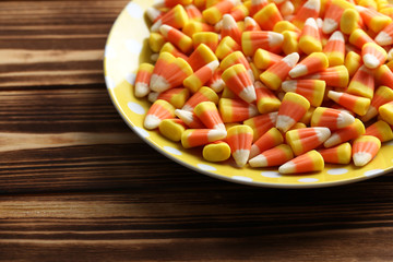 Halloween candy corns in plate on brown wooden background