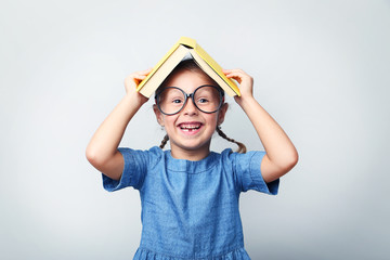 Portrait of little girl with glasses and book on grey background